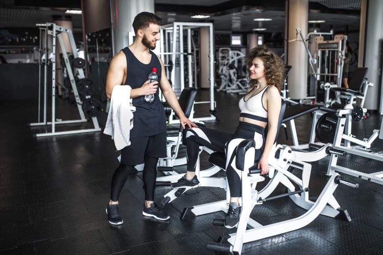 A handsome fitness instructor is helping his attractive client learn how to work out at the local gym.
