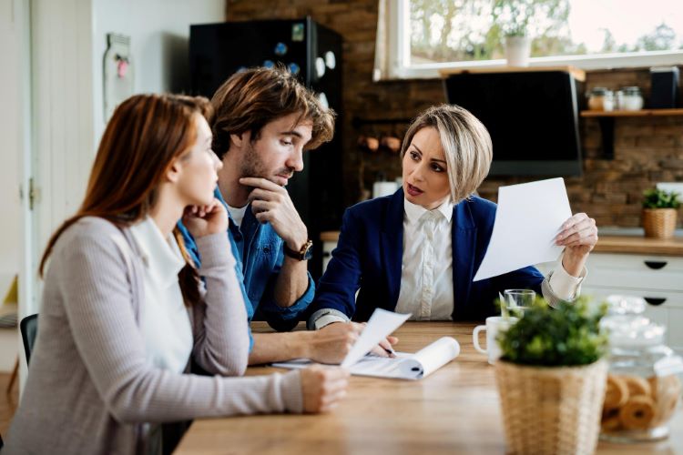 Financial advisor communicating with young couple while going through their financial reports during a meeting at home