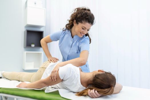 Young woman doctor chiropractor or osteopath fixing lying womans back with hands movements during visit in manual therapy clinic professional chiropractor during work