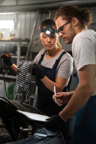 Male and female auto electricians working in the shop on a car